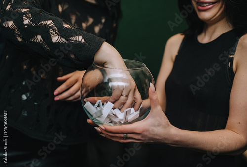 Woman picking paper, lottery, random ticket from glass jar with hand while playing game at party.