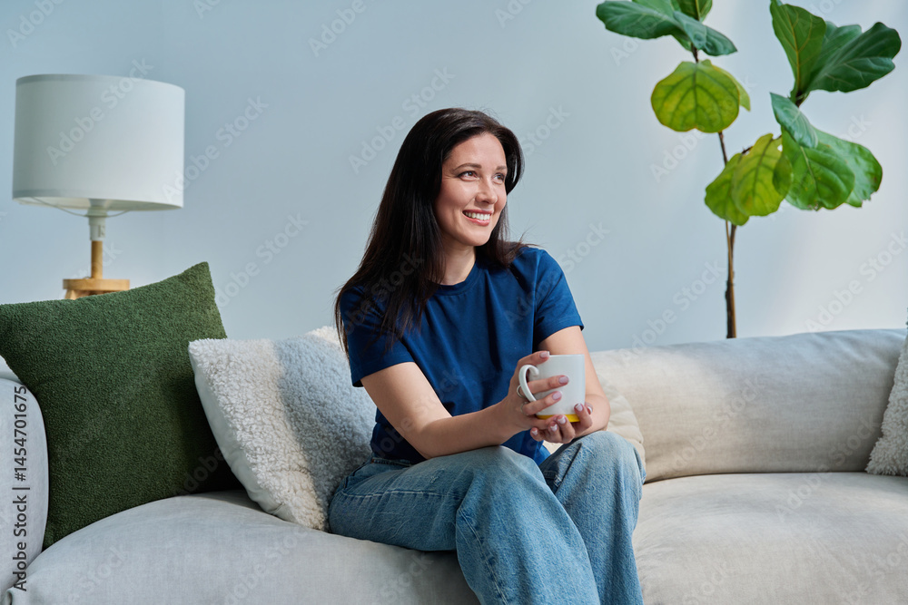 Portrait of beautiful smiling young brunette woman sitting on sofa in living room