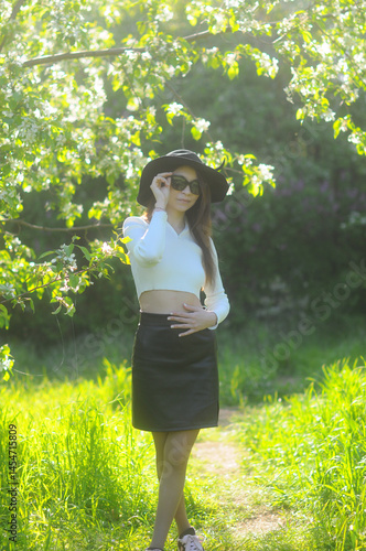 young girl walking in a summer park in a black hat in a white blouse and skirt