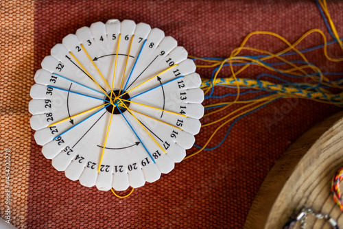  A braiding disk with blue and yellow threads is in the process of creating a patterned bracelet