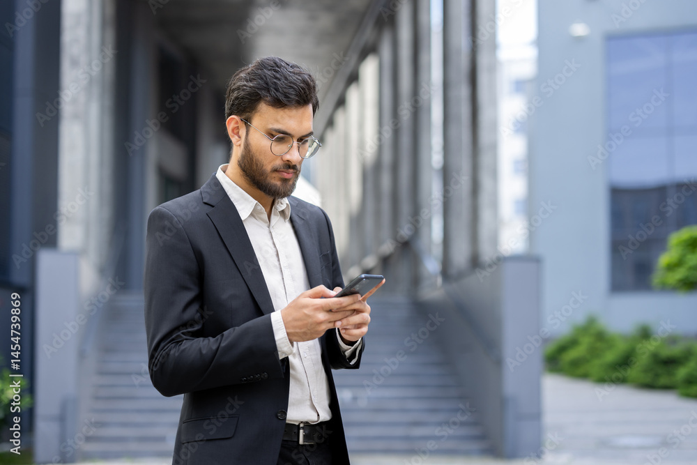 A businessman in a suit looks intently at his smartphone while standing outside a modern office building. He appears focused on the content.