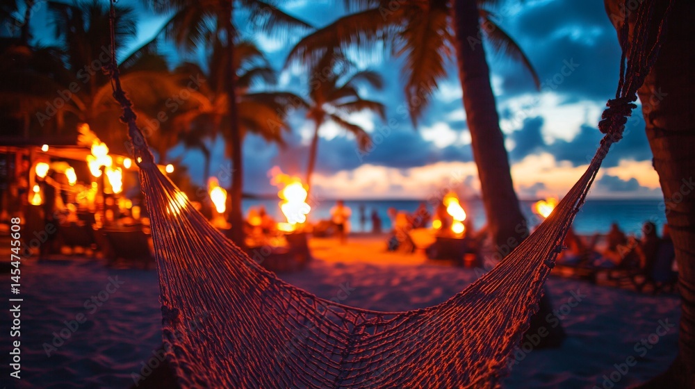 Close up of hammock mesh stretched between palm trees, tiki torches and beach party in background