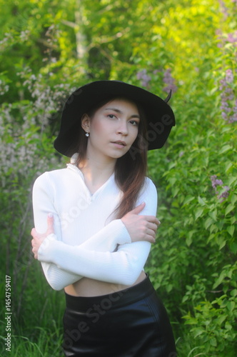 young girl walking in a summer park in a black hat in a white blouse and skirt