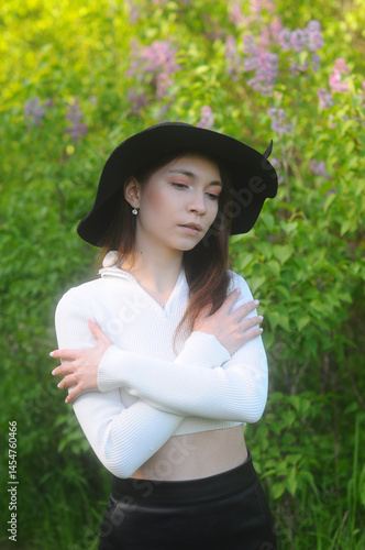 young girl walking in a summer park in a black hat in a white blouse and skirt