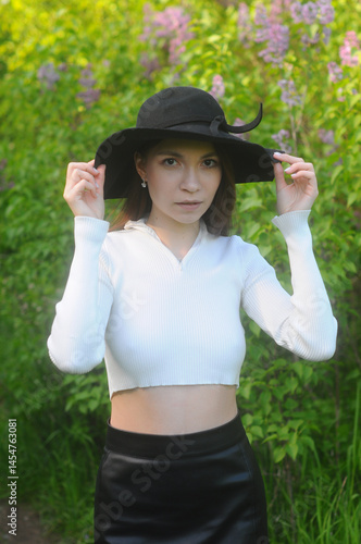 young girl walking in a summer park in a black hat in a white blouse and skirt