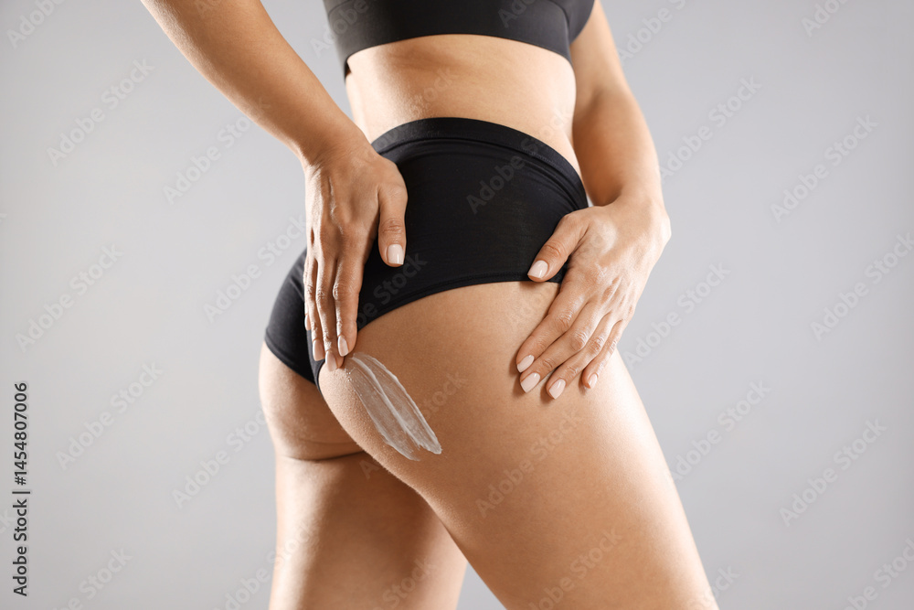 Fototapeta premium Woman applying anti cellulite cream on grey background, closeup