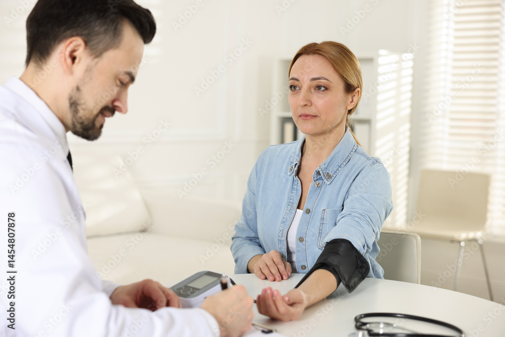 Fototapeta premium Cardiologist measuring patient's blood pressure at table in hospital