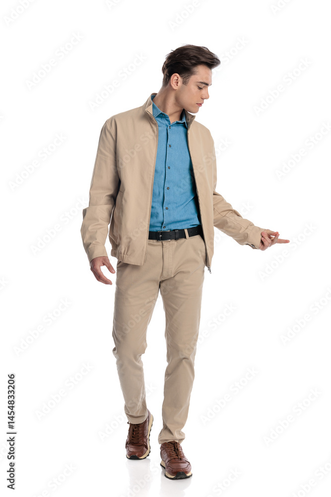 Fototapeta premium sexy fashion guy in beige jacket looking down side and walking