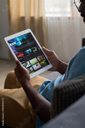 Foto Vertical medium shot of African American man sitting on couch at home, watching