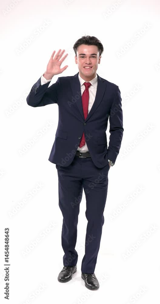 vertical video of happy young man in navy blue suit holding one hand in pocket and waving with the other, smiling and being excited in front of white background vertical video of happy young man in navy blue suit holding one hand in pocket and waving with the other, smiling and being excited in front of white background