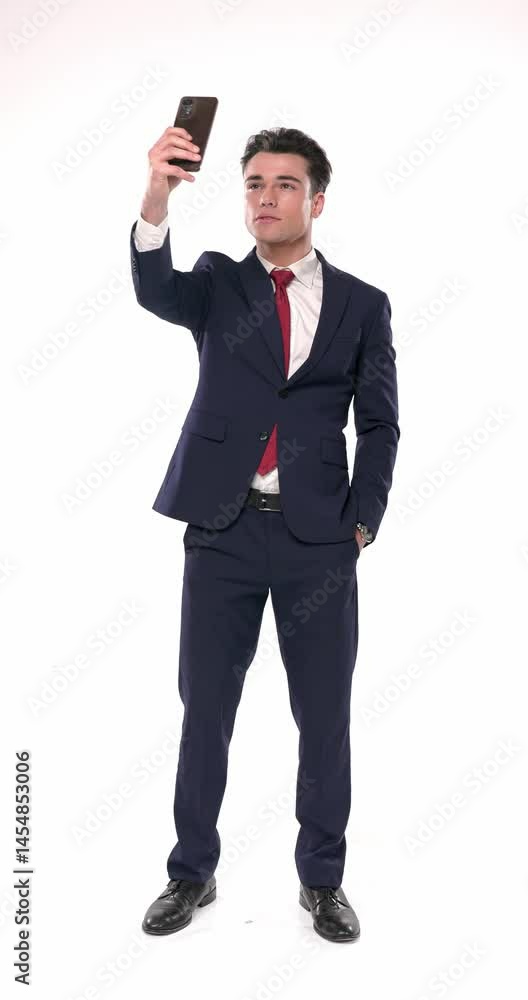 sexy elegant man in navy blue suit holding telephone up and taking a selfie while holding one hand in pocket in front of white background sexy elegant man in navy blue suit holding telephone up and taking a selfie while holding one hand in pocket in front of white background