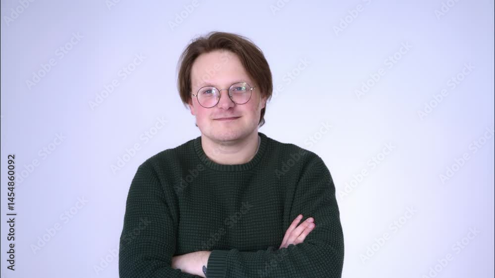 A portrait of a young man with blue eyes and light brown hair, wearing glasses and a green sweater, smiling and laughing against a light background.