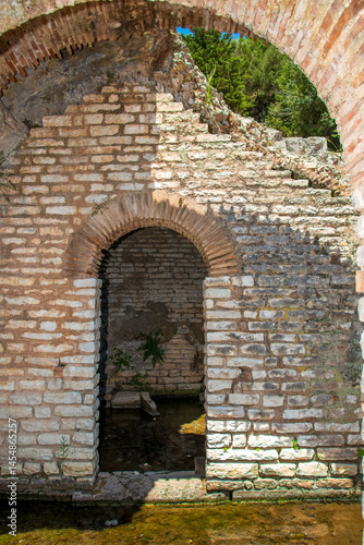 Wallpaper Mural Sunlit ancient limestone archway at the edge of a reflective water channel within the archaeological ruins of Butrint in southern Albania Torontodigital.ca