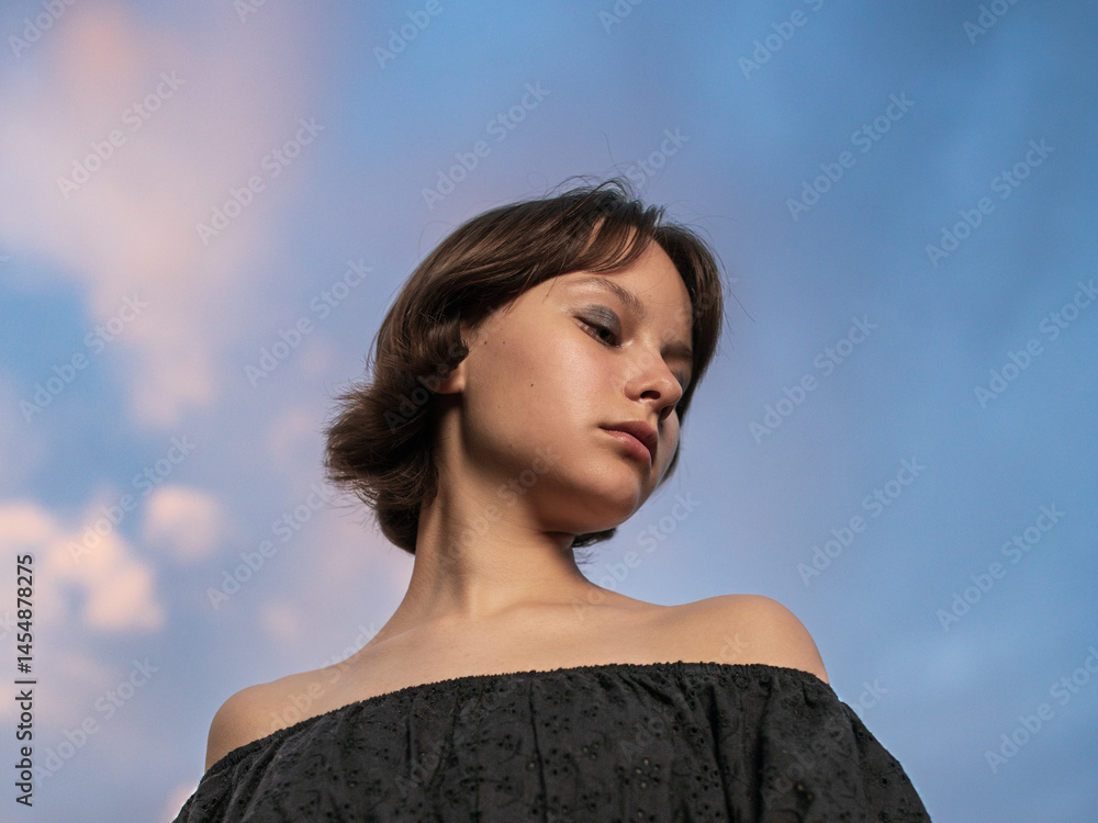 Portrait of beautiful serious teen girl against cloudy sky