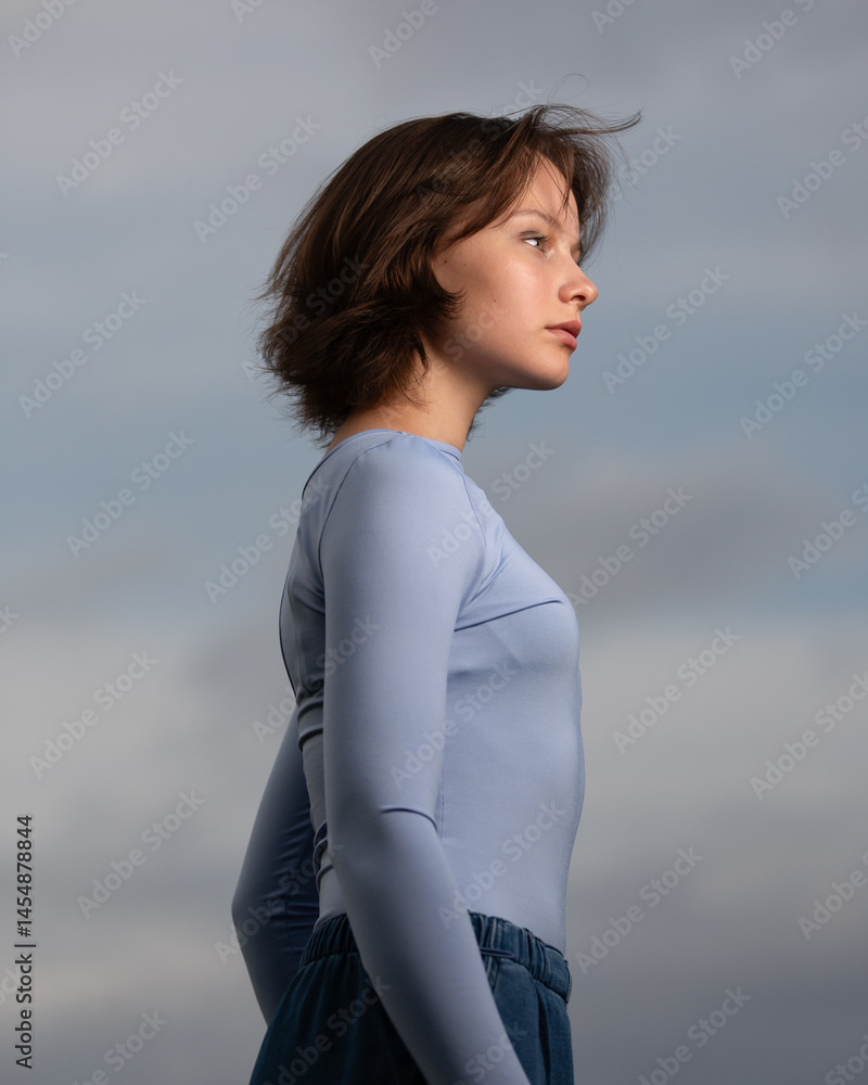 Portrait of beautiful serious teen girl against cloudy sky on windy day