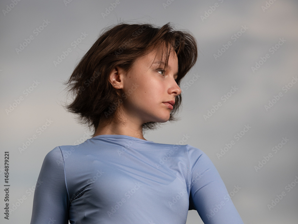 Portrait of beautiful serious teen girl against cloudy sky on windy day