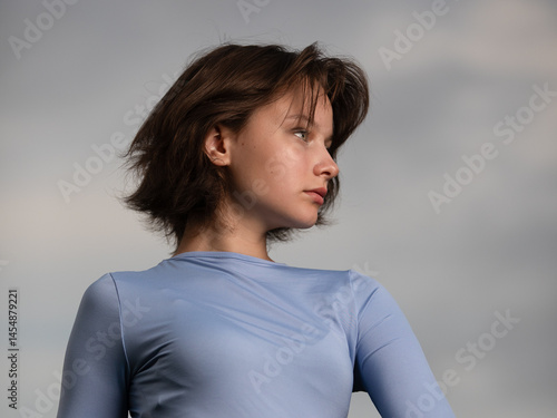 Portrait of beautiful serious teen girl against cloudy sky on windy day