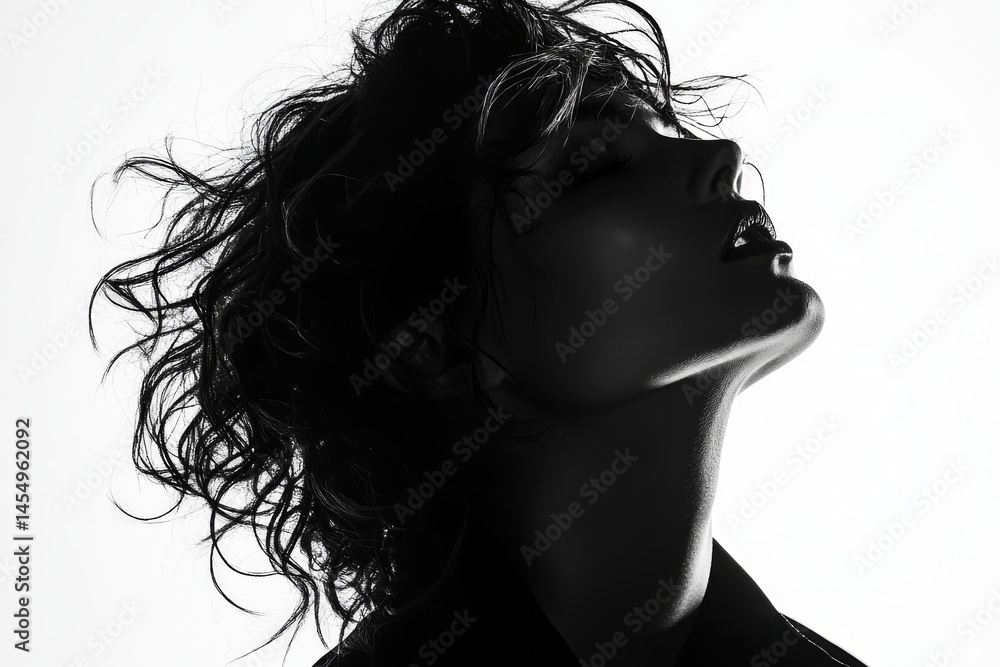 In a dark studio, a portrait image captures a woman standing with her back to the viewer, silhouetted against a white background on a pastel grey background