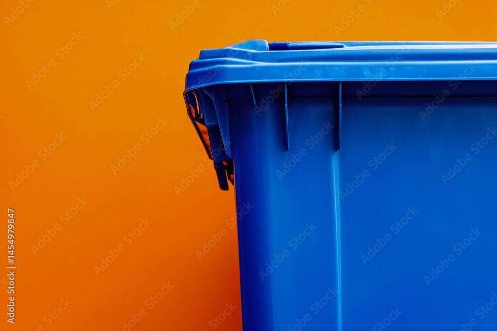 Close-up of a blue waste bin with a dark lid against an orange background