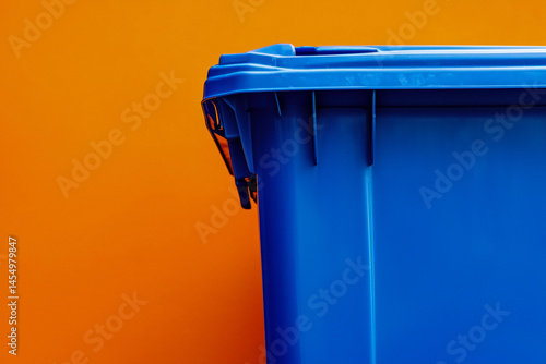 Obraz na płótnie Close-up of a blue waste bin with a dark lid against an orange background w salonie
