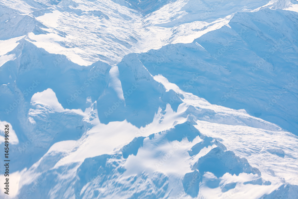 Vast expanse of snow covered mountains stretches across rugged peaks and deep valleys under a clear sky. Pristine white landscape, captured from an aerial perspective