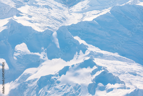 Obraz na płótnie Vast expanse of snow covered mountains stretches across rugged peaks and deep valleys under a clear sky. Pristine white landscape, captured from an aerial perspective w salonie