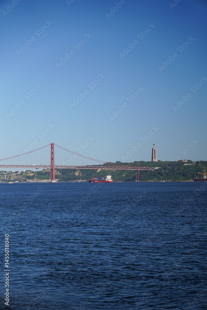 Fototapeta premium Scenic View of Suspension Bridge Cargo Ship and Monument on Calm Water