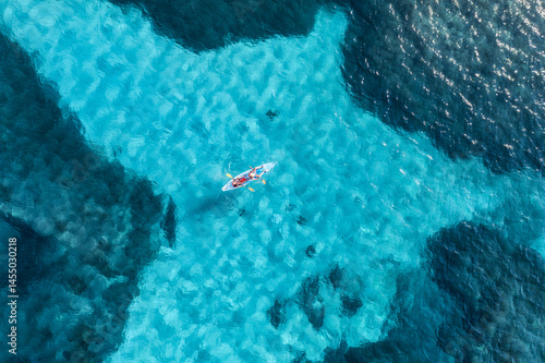 Canvas Print Aerial view of a kayaker paddling through vibrant turquoise shallow waters surrounded by deep blue ocean, creating a breathtaking contrast and showcasing the beauty of a tropical paradise