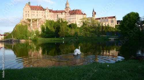 Castle overlooks serene lake with swan gliding gracefully amidst lush green landscape in evening light