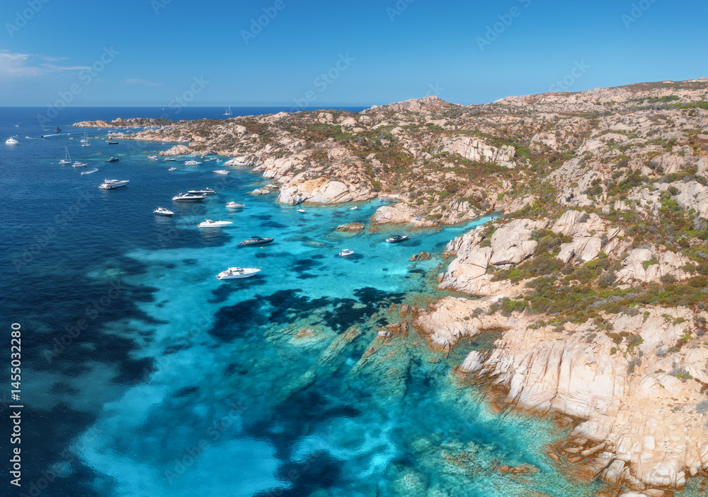Fototapeta premium Breathtaking aerial view capturing luxury yachts moored along the rocky coastline of la maddalena archipelago in sardinia island, revealing vibrant turquoise waters. Top view of boats and blue sea