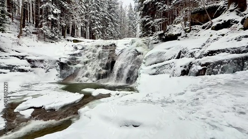 A frozen mountain river with a waterfall in a winter forest