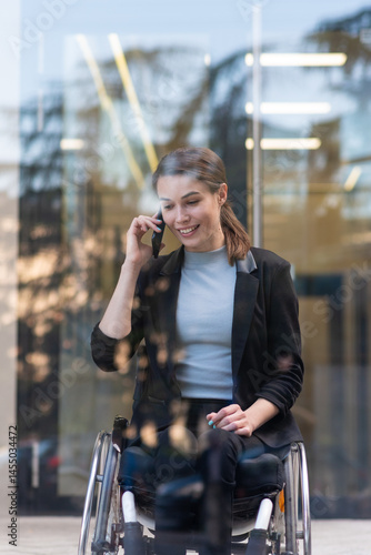 Smiling businesswoman in wheelchair using smart phone near office building