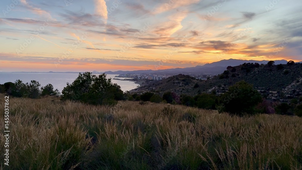 Obraz premium Experience the stunning coastal view at sunset, complemented by picturesque rolling hills nearby