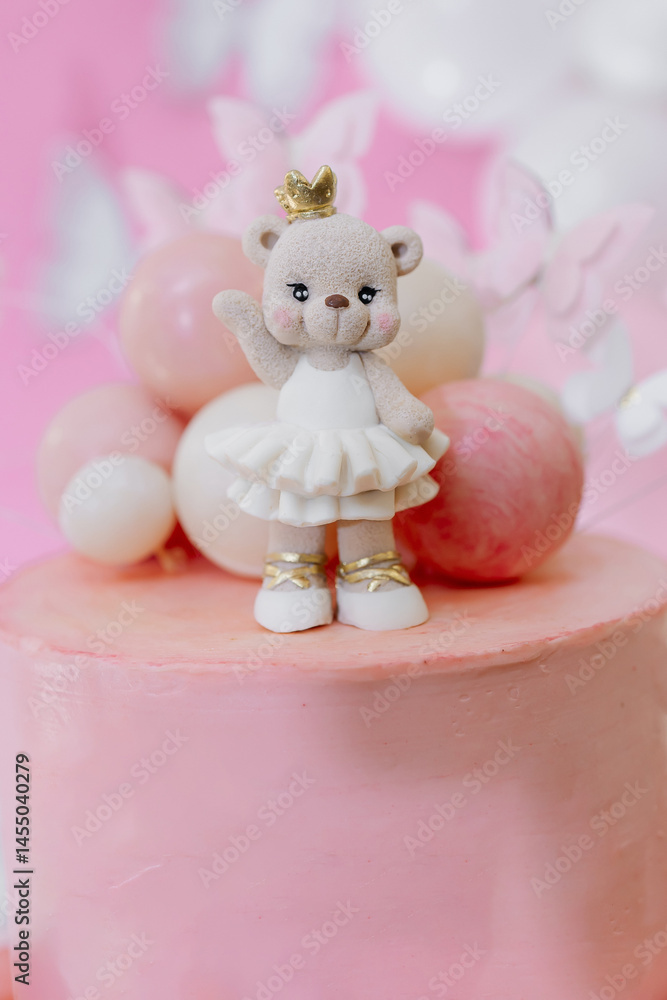 Pink first birthday cake with teddy bear figurine. Soft pastel colors and festive decoration create a warm, festive atmosphere. Sweet cake for a one-year-old birthday girl