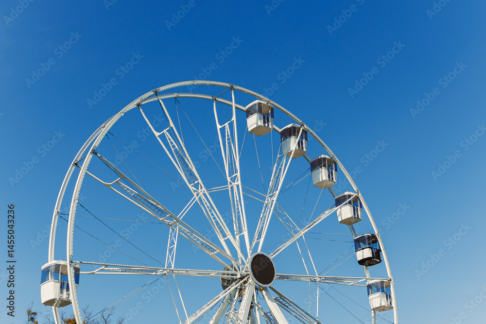 A large Ferris wheel against a blue sky. Cabins on the Ferris wheel.