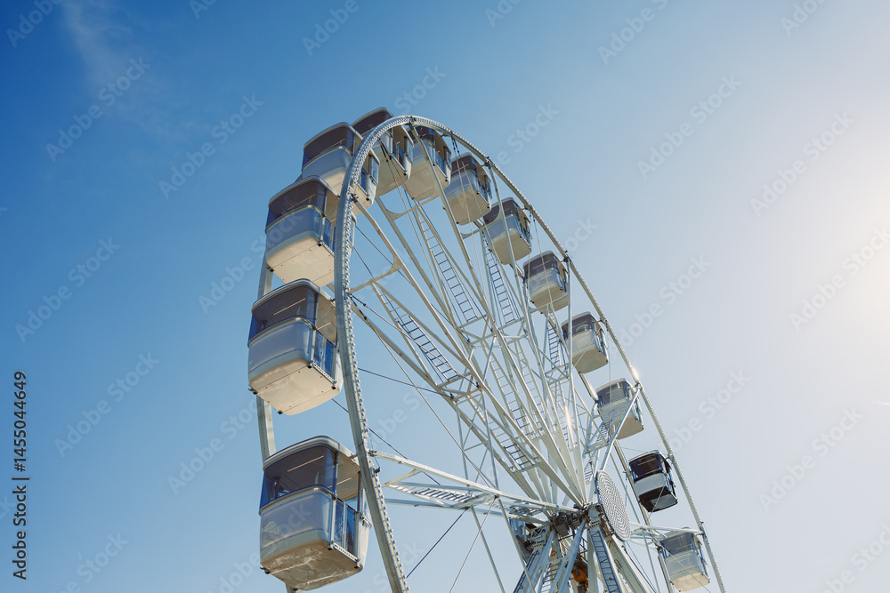 A large Ferris wheel rises into the air with cabins against a blue sky. A Ferris wheel with enclosed cabins.