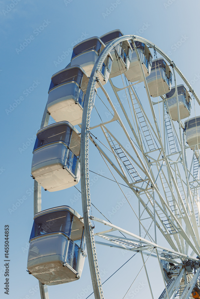 A large Ferris wheel rises into the air with cabins against a blue sky. A Ferris wheel with enclosed cabins.