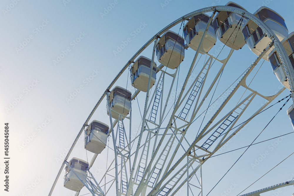 An attraction for viewing the city from above. A large Ferris wheel rises into the air with cabins against a blue sky. A Ferris wheel with closed cabins.