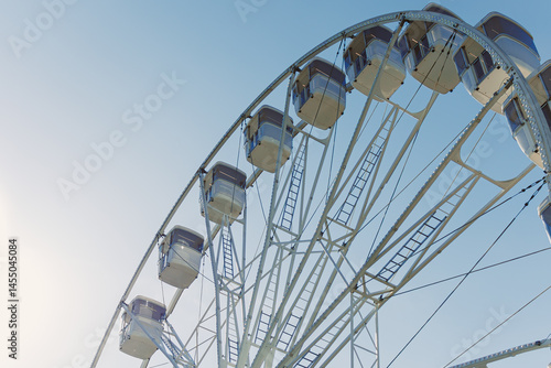 Obraz na płótnie An attraction for viewing the city from above. A large Ferris wheel rises into the air with cabins against a blue sky. A Ferris wheel with closed cabins. w salonie