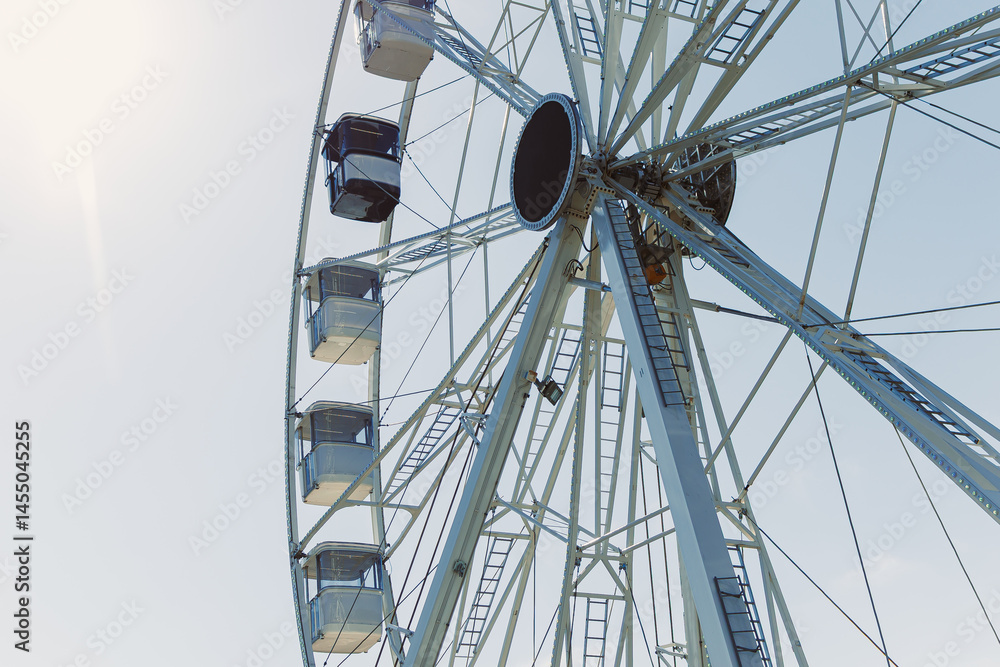 An attraction for viewing the city from above. A large Ferris wheel rises into the air with cabins against a blue sky. A Ferris wheel with closed cabins.