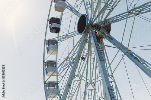 Obraz na płótnie An attraction for viewing the city from above. A large Ferris wheel rises into the air with cabins against a blue sky. A Ferris wheel with closed cabins. w salonie