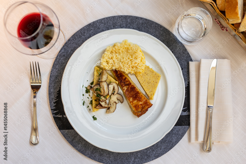 A beautifully plated serving of Frico and polenta, typical of Friuli Venezia Giulia, sits on a restaurant table with cutlery and a placemat, ready to be enjoyed. A beautifully plated serving of Frico and polenta, typical of Friuli Venezia Giulia, sits on a restaurant table with cutlery and a placemat, ready to be enjoyed.