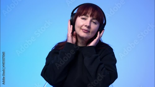 A portrait of a young red-haired woman with blue eyes wearing headphones, listening to music and nodding her head to the rhythm.