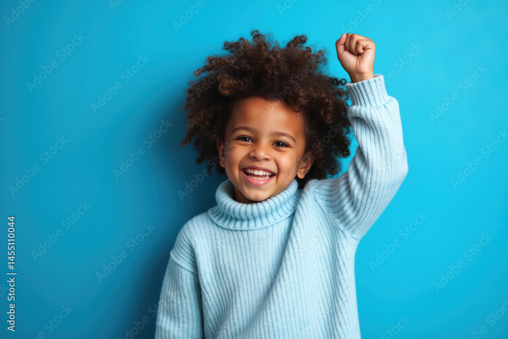 A smiling child with curly hair, wearing a light blue sweater, stands against a blue background with a raised fist.