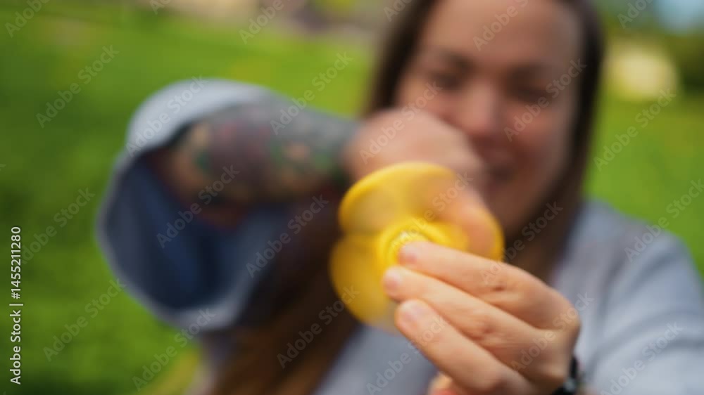 A cheerful young person joyfully spins a bright yellow fidget spinner outdoors, surrounded by beautiful nature
