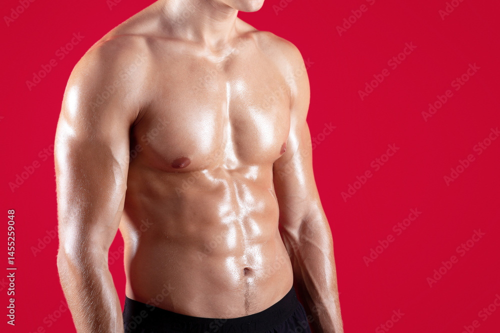 Fototapeta premium Closeup view of young strong sportsman with naked torso and prominent abs muscles on red studio background. Fit millennial guy with sexy body, cropped view. Strength workout concept