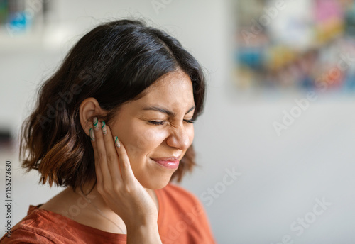 Sick young arab woman having ear pain at home, upset middle eastern female rubbing sore auricle with hand and frowning, suffering from otitis and acute ache, closeup shot with copy space