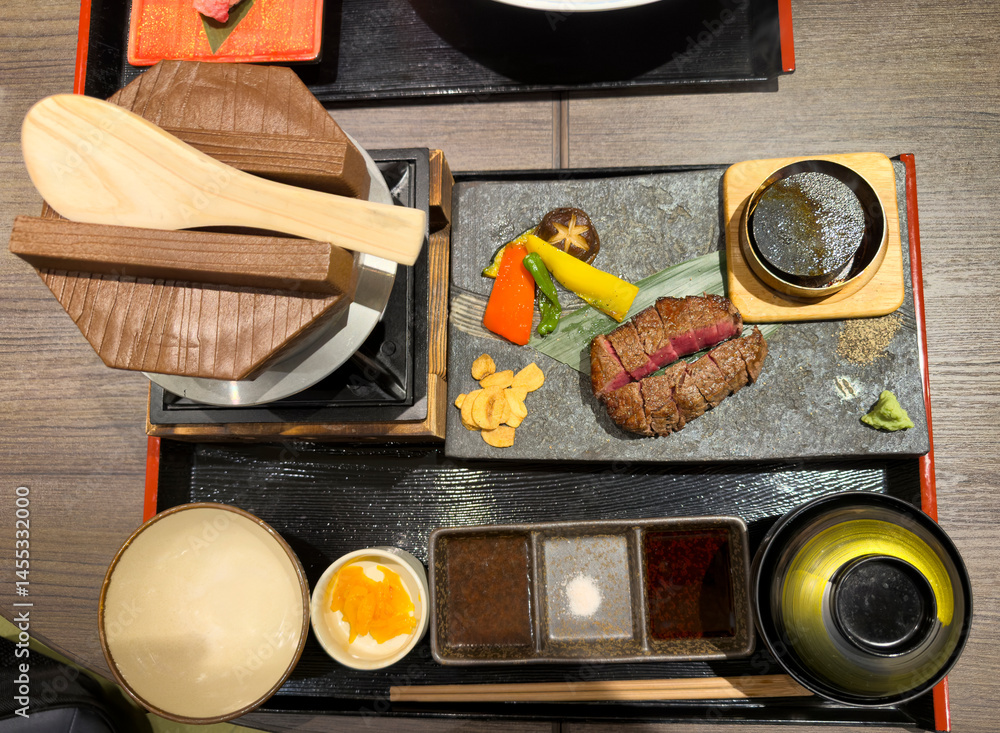 Wagyu beef steak sliced into pieces on stone cutting board with barbecued vegetables in overhead view