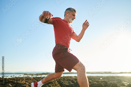 Senior man running on the beach wearing sport clothes and earphones