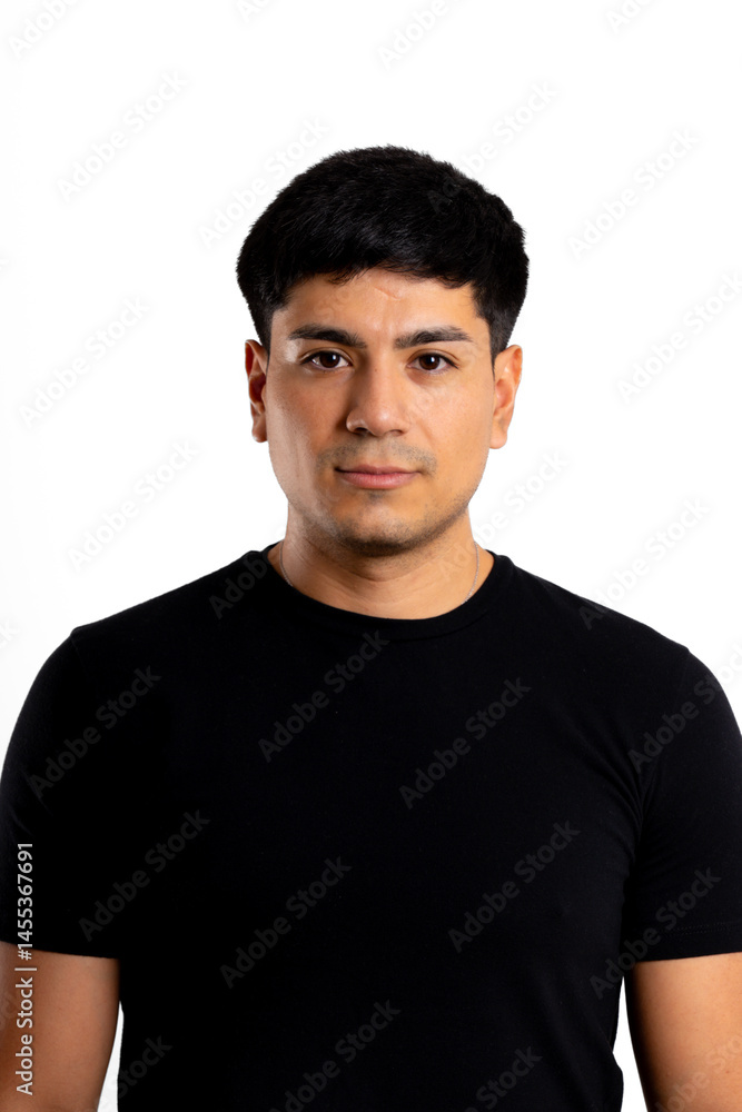 Fototapeta premium Portrait of a young Latin man looking seriously at the camera, dressed in black with a white background